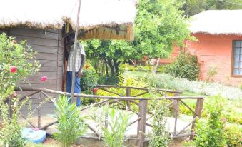 a man standing next to a small house with a thatched roof , surrounded by lush greenery at Lalanasi Lodge