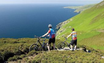 a group of people riding bicycles on a grassy hillside , overlooking the ocean and mountains at Trail Lodge