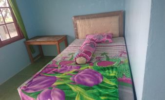 a bed with a colorful blanket and a stuffed animal on the bedside table in a small room at Penginapan Rindu Alam Soala Gogo