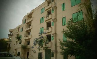 a beige building with green windows and balconies , surrounded by trees and a car parked outside at Parkway Apartments