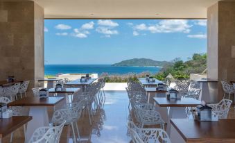 a restaurant with white tables and chairs , overlooking a beautiful view of the ocean and mountains at Wyndham Tamarindo