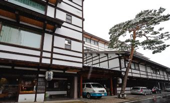 a snow - covered street with a wooden building on one side and a car parked in front of it at Osakaya Ryokan