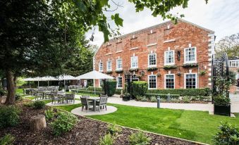 a brick building with multiple windows and balconies , surrounded by greenery and umbrellas on a grassy lawn at The Knaresborough Inn - the Inn Collection Group