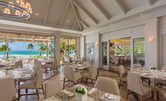 a large , elegant dining room with multiple tables and chairs arranged for a group of people to enjoy a meal at The St. Regis Bahia Beach Resort, Puerto Rico