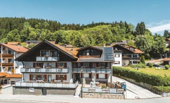 a large , two - story house with a sloping roof and a balcony , surrounded by trees and mountains at Hotel Haus am See