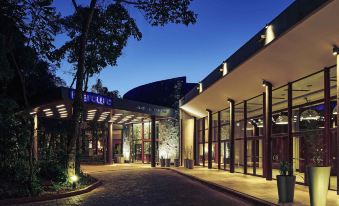 a large building with a lit - up entrance and walkway , surrounded by trees and lit up at night at Mercure Iguazu Hotel Iru