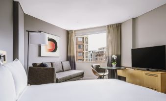 a modern hotel room with a large bed , couch , and flat screen tv , all situated in front of a window at Novotel Sydney Darling Harbour