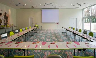 a conference room with long tables and chairs arranged in rows , along with a projector screen mounted on the wall at Semiramis