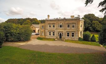 a large , two - story building with a courtyard and parking lot in front of it , surrounded by trees and grass at Cleatham Hall