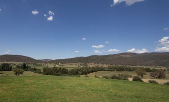 a vast green field with a clear blue sky and distant mountains , accompanied by a few small buildings at Stay in Mudgee
