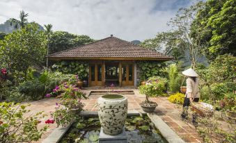 a man standing in front of a house , surrounded by lush greenery and a pond at Tam Coc Garden Resort