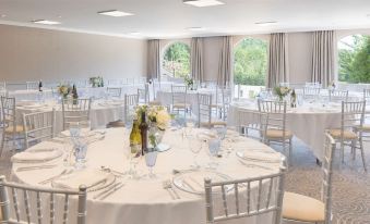 a well - decorated banquet hall with several round tables covered in white tablecloths and adorned with wine glasses at Hilton Cobham