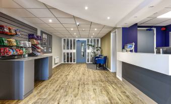 a modern office reception area with wooden floors , blue walls , and a blue reception desk at Days Inn by Wyndham London Stansted Airport