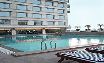 a swimming pool surrounded by a hotel , with lounge chairs placed around the pool for relaxation at Hyatt Centric Janakpuri New Delhi