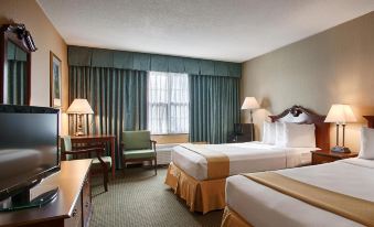 a hotel room with two beds , a tv , and lamps , as well as a window with blue curtains at Clarion Inn Falls Church- Arlington
