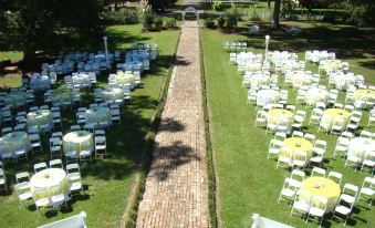 a long brick walkway is surrounded by white and yellow chairs set up for an outdoor wedding at Blythewood Plantation