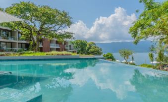 a large swimming pool surrounded by trees , with a building in the background and a lake visible at Wyndham Ilhabela Casa di Sirena