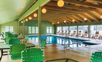 a large indoor swimming pool with green and blue chairs , surrounded by a wooden ceiling at Woodwards White Mountain Resort, BW Signature Collection