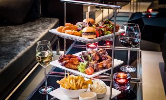 a dining table with a three - tiered tray filled with various food items , including burgers , fries , and wine glasses at Park Plaza Westminster Bridge London