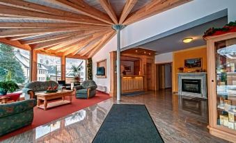 a spacious living room with wooden ceiling and walls , featuring a couch , chairs , and a fireplace at Hotel am Kurpark