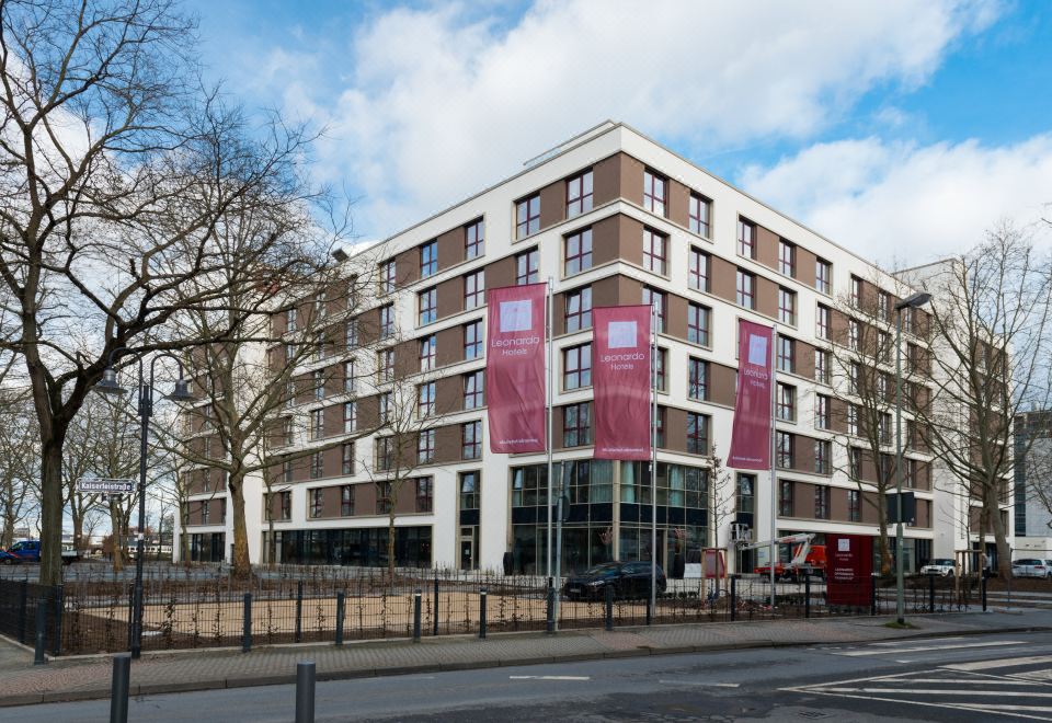 a large building with pink and white banners on the side , located in a city setting at Leonardo Offenbach Frankfurt