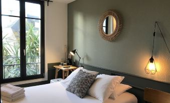 a bedroom with a large bed and a round mirror on the wall , creating a cozy atmosphere at Hotel de France