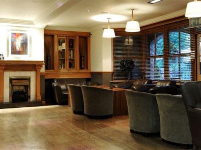 a well - lit room with wooden floors , leather couches , and a fireplace , decorated with trees and windows at Village Hotel Liverpool