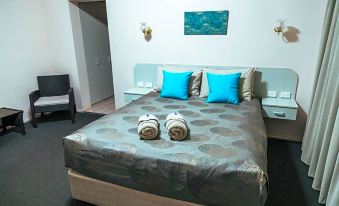 a well - arranged hotel room with a bed , blue pillows , and towels , along with a wall - mounted lamp at Copper City Motel