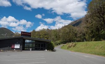a building with a red sign is located next to a parking lot and mountain at Maruia Hot Springs
