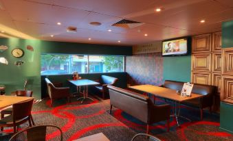 a modern , stylish restaurant with green walls and red carpet , containing multiple dining tables and couches , as well as a tv screen on the at Prince of Wales Hotel