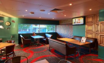 a modern , well - lit restaurant with green walls and red flooring , featuring multiple tables and chairs arranged in a lounge - like setting at Prince of Wales Hotel