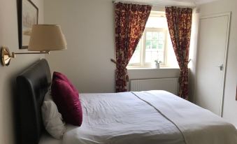 a well - lit bedroom with a white bed , red curtains , and a lamp on the nightstand at The Barford Inn