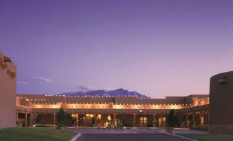 a large building with a driveway and a mountain in the background at dusk , illuminated by lights at Hyatt Regency Tamaya Resort and Spa