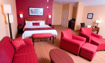 a hotel room with a red and white color scheme , featuring a king - sized bed , a couch , and a tv at Courtyard Middlebury