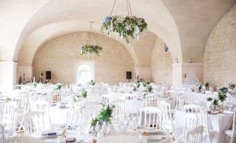 a white dining room with tables and chairs set up for a wedding reception , featuring greenery hanging from the ceiling at Chateau de la Bourdaisiere
