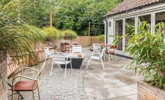 a paved courtyard with several chairs and tables arranged for outdoor dining , surrounded by greenery at The Litton
