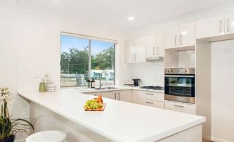 a modern kitchen with white cabinets , a large island with a fruit bowl on it , and a stainless steel oven at Beachfront Hallidays Point
