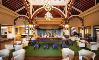 a large hotel lobby with multiple seating areas , including couches , chairs , and a bar , as well as a chandelier hanging from the ceiling at Royal Palms Beach Hotel