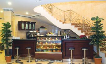 The restaurant features a bar with stairs and a counter where food is displayed in front at Emaar Grand Hotel