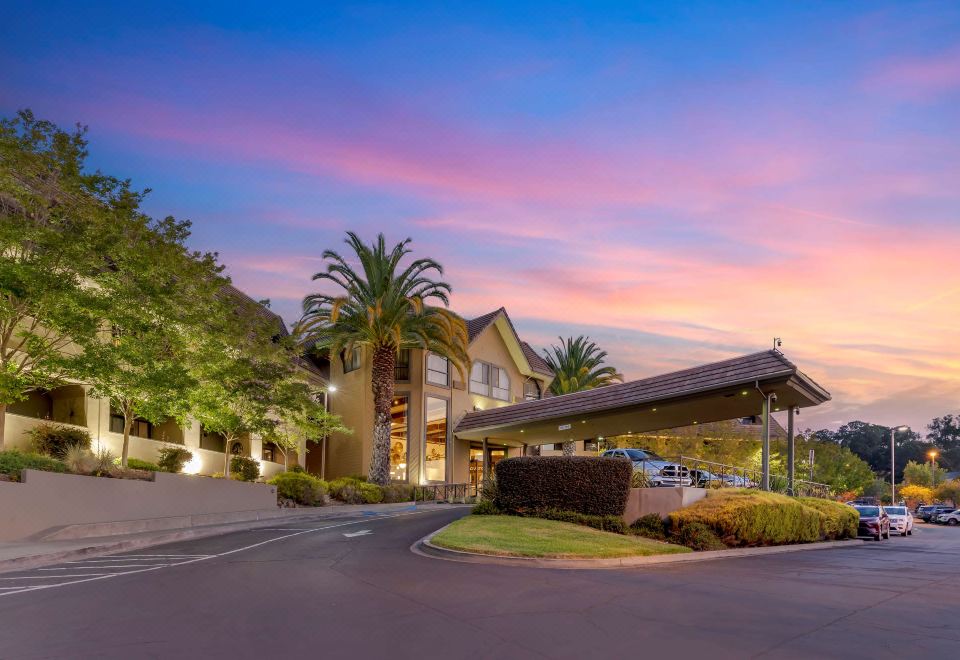 a large building with palm trees and a car parked in front , under a beautiful sunset sky at Best Western Plus Novato Oaks Inn