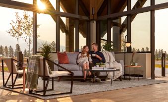 a man and a woman are sitting on a couch in a room with large windows , enjoying each other 's company while they watch a movie on at Forest Park Hotel