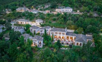 a large villa complex with multiple buildings and trees , set against a mountainous backdrop , under a clear blue sky at Aristi Mountain Resort