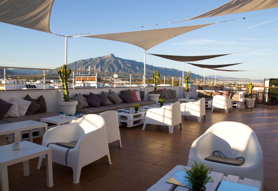 a rooftop patio with white couches and chairs arranged for guests to enjoy the view of a mountain in the distance at NH San Pedro