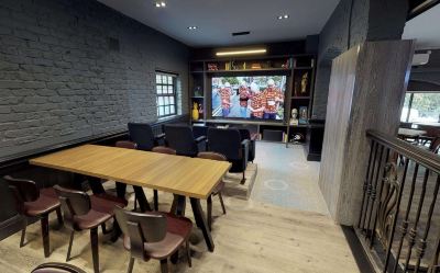 a large screen is mounted on a brick wall in a room with wooden furniture at Village Hotel Liverpool