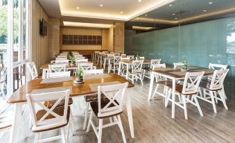 a large dining room with white wooden tables and chairs , arranged in a restaurant setting at Novena Hotel Bandung