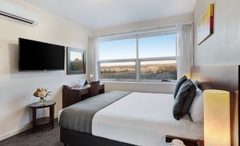 a large bed with a white comforter and black headboard is in a hotel room with a window at Quest Mawson Lakes
