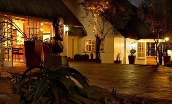 a house with a thatched roof and large windows is lit up at night , surrounded by plants at Summerhill Guest Estate