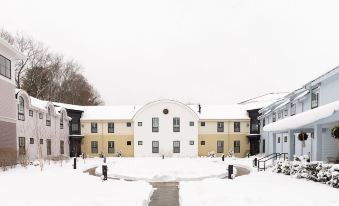 a snow - covered courtyard with two buildings , one of which appears to be a church and another similar building , surrounded by trees at Briar Barn Inn