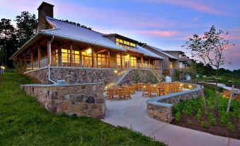 a large house with a stone exterior and wooden patio furniture is shown at dusk at Nature Inn at Bald Eagle