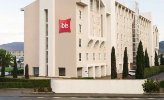 a large , white building with a red sign on the side and green bushes in front at Ibis Firenze Nord Aeroporto